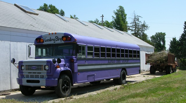 Purple schoolbus by shed with grain truck